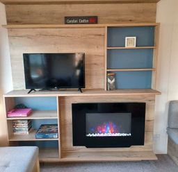 a wooden entertainment unit with a TV and electric fireplace at Hafan y Mor Haven - Holiday Accommodation 12637 in Pwllheli