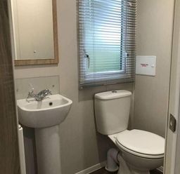 a small bathroom with a sink, toilet, and window at Kelling Heath Holiday Park - Holiday Accommodation 13133, Holt