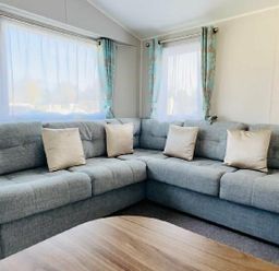 a gray sectional sofa with pillows and windows covered with curtain at Butlins Minehead - Holiday Accommodation 13288 Minehead