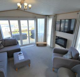 a living room with a sofa, armchair, coffee table, television, and large windows at Perran Sands - Holiday Accommodation 15012, Perranporth