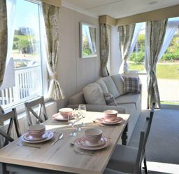 a dining area with a table set for four and a sofa near large windows at Perran Sands - Holiday Accommodation 15554 Perranporth