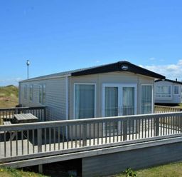 a holiday caravan with a deck and picnic table at Perran Sands - Holiday Accommodation 15598 in Perranporth