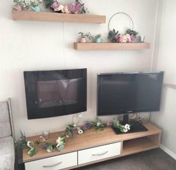 a wall-mounted TV and a separate TV on a unit with floral decorations at Hafan y Mor Haven - Holiday Accommodation 15817 Pwllheli