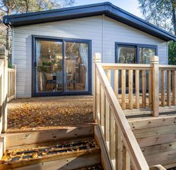 a wooden deck leading to a cabin with large glass doors at Kelling Heath Holiday Park - Holiday Accommodation 16221 in Holt