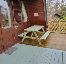 a wooden picnic table on a deck outside a cabin at Hafan y Mor Haven - Holiday Accommodation 16279 Pwllheli
