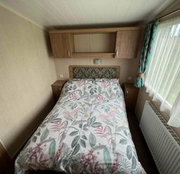 a bedroom with a double bed covered in floral bedding and a window at Hafan y Mor Haven - Holiday Accommodation 17436 Pwllheli