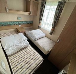 a bedroom with two single beds, a bedside table, and curtains at Hafan y Mor Haven - Holiday Accommodation 17436 in Pwllheli