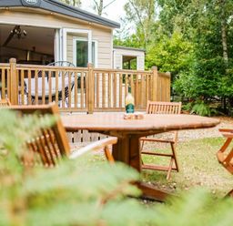 a wooden table and chairs with a view of a cabin and trees at Kelling Heath Holiday Park - Holiday Accommodation 18664 in Holt