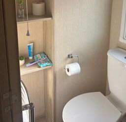 A bathroom with a toilet and shelf containing toiletries at Southview Holiday Park - Holiday Accommodation 19123, Skegness