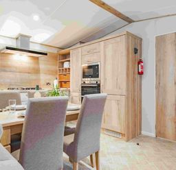 a kitchen and dining area with wooden cabinets and a table at Kelling Heath Holiday Park - Holiday Accommodation 19669, Holt
