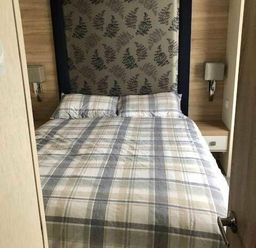 a bedroom with a checked bedspread and two pillows at Pinewoods Holiday Park - Holiday Accommodation 19734 in Wells-Next-The-Sea