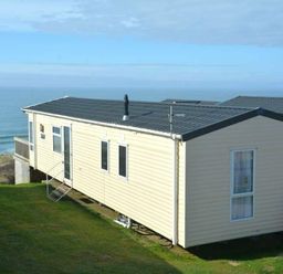 a holiday home with a grassy area and ocean view at Perran Sands - Holiday Accommodation 19778 Perranporth