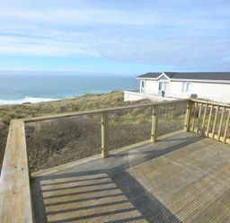 a deck with a view of the ocean and a building in the background at Perran Sands - Holiday Accommodation 19778 Perranporth