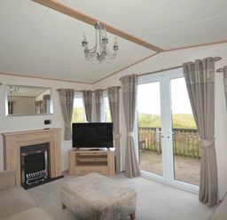 a living room with a sofa, television, chandelier, and doors leading to an outdoor area at Perran Sands - Holiday Accommodation 20514, Perranporth