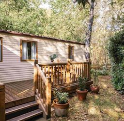 a holiday cabin with a wooden deck and potted plants at Kelling Heath Holiday Park - Holiday Accommodation 20958 in Weybourne