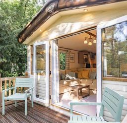 a deck with two chairs leading to a cabin with large windows at Kelling Heath Holiday Park - Holiday Accommodation 20958 Weybourne