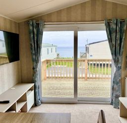 a living room with a TV and curtains overlooking a balcony at Perran Sands - Holiday Accommodation 21088 in Perranporth