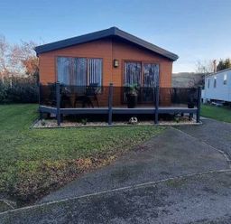 a cabin with a wooden deck surrounded by grass at Presthaven Beach Resort - Holiday Accommodation 21358 in Prestatyn