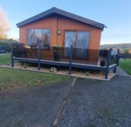 a cabin with a deck and glass railing surrounded by grass at Presthaven Beach Resort - Holiday Accommodation 21358, Prestatyn