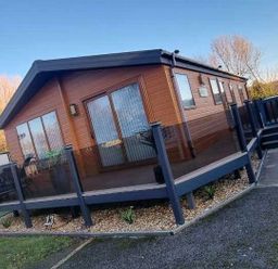 a wooden lodge with large windows and a deck area at Presthaven Beach Resort - Holiday Accommodation 21358, Prestatyn