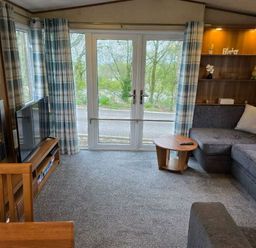 a living room with a gray sofa, wooden furniture, and large windows at Beacon Fell View Holiday Park - Holiday Accommodation 21653 Preston