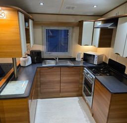 a kitchen with wooden cabinets, a sink, stove, and appliances at Beacon Fell View Holiday Park - Holiday Accommodation 21653, Preston