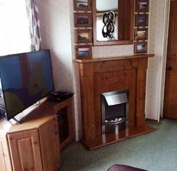 a living room with a wooden fireplace and a TV on a stand at Hafan y Mor Haven - Holiday Accommodation 21715 in Pwllheli