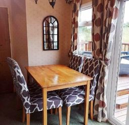 a dining area with a wooden table and patterned chairs at Hafan y Mor Haven - Holiday Accommodation 21715 Pwllheli