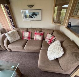 a beige sectional sofa with red plaid cushions and white throw pillows at Clarach Bay Holiday Village - Holiday Accommodation 21850, Aberystwyth