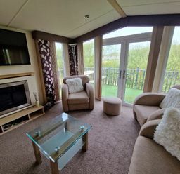 a living room with a television, sofa, armchair, coffee table, and patio doors at Clarach Bay Holiday Village - Holiday Accommodation 21850, Aberystwyth