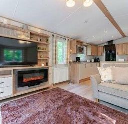 a living room with a large TV, fireplace, and kitchen area at Kelling Heath Holiday Park - Holiday Accommodation 22244, Holt