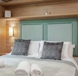 a bedroom with a double bed, decorative pillows, and wooden shelving at Kelling Heath Holiday Park - Holiday Accommodation 22244, Holt