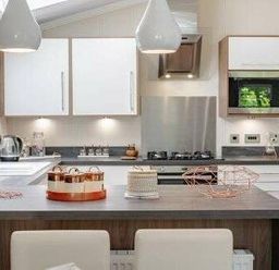a modern kitchen with white cabinets, a stainless steel sink, and pendant lights at Kelling Heath Holiday Park - Holiday Accommodation 22249 in Holt