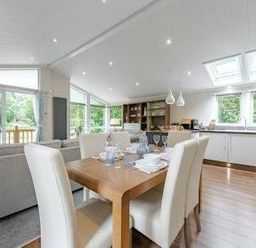 a dining area with a wooden table set for a meal and a modern kitchen at Kelling Heath Holiday Park - Holiday Accommodation 22249, Holt