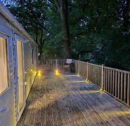 a wooden deck with lights and a chair surrounded by trees at Aberdunant Hall Holiday Park - Holiday Accommodation 22358 in Porthmadog