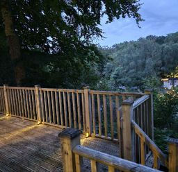 a wooden deck with a railing overlooking trees at Aberdunant Hall Holiday Park - Holiday Accommodation 22358 in Porthmadog