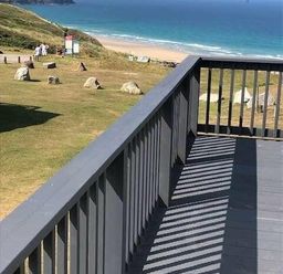 a view from a balcony overlooking a beach with grass and rocks at Perran Sands - Holiday Accommodation 7528, Perranporth, Cornwall, United Kingdom