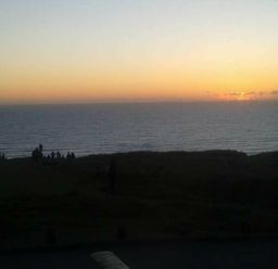 a sunset over the ocean with people sitting on the shore at Perran Sands - Holiday Accommodation 8131 Perranporth