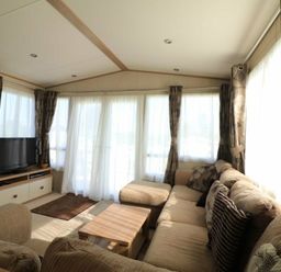 a living room with a sofa, television, and large windows with curtains at White Acres Holiday Park - Holiday Accommodation 895, Newquay