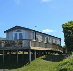a mobile home with a wooden deck situated on grassy terrain at Perran Sands - Holiday Accommodation 8982 Perranporth