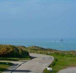 a coastal view with a road leading to the sea and distant rocks at Perran Sands - Holiday Accommodation 8982, Perranporth