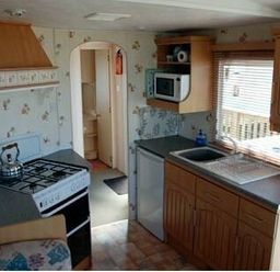 a kitchen with cabinets, a stove, microwave, and sink at Perran Sands - Holiday Accommodation 9159, Perranporth