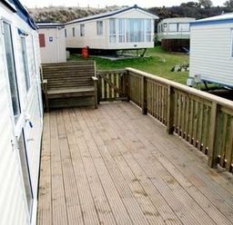 a wooden deck area with a bench and nearby caravans at Perran Sands - Holiday Accommodation 9159, Perranporth