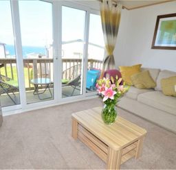 a living room with a sofa, coffee table, and large windows overlooking the sea at Perran Sands - Holiday Accommodation 9657 Perranporth
