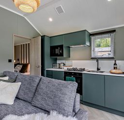 A kitchen with green cabinets and a sofa at Prion Spa, Llandyrnog