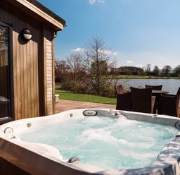 An outdoor area with a hot tub and seating near a lake at Lawson in Wigton