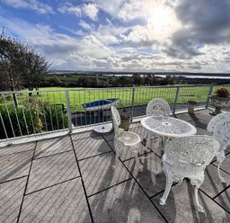 An outdoor seating area with a table and chairs overlooking a green landscape at Ty Nain in Bodorgan