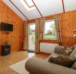 A snug room with a sofa and television at The Log Cabin in Corse near Gloucester