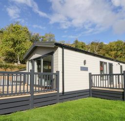 A mobile home with a deck and grass area at Altair Lodge
