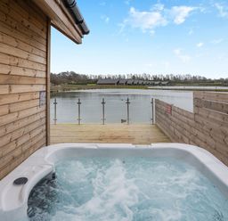 A hot tub on wooden decking overlooking water at Tranquillity 3 in Warton near Carnforth